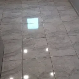 Ułożona podłoga z szarych, kwadratowych płytek imitujących marmur, widoczne odbicie światła na powierzchni.