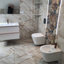 Artur Olejarnik - Wykończona łazienka z płytkami imitującymi marmur, podświetleniem LED, wiszącą toaletą i bidetem. W lustrze odbija się fotograf.