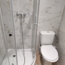 Artur Olejarnik - Wykończona łazienka: kabina prysznicowa z brodzikiem i toaleta w jasnych, marmurkowych płytkach. Widok na armaturę i detale wykończenia.