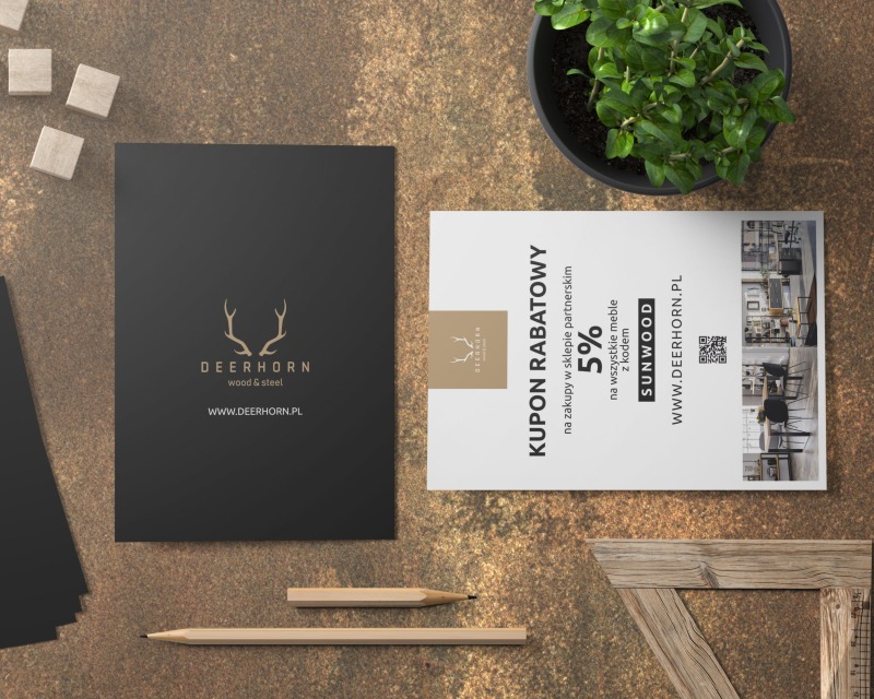 Makieta materiałów reklamowych firmy Deerhorn: czarne wizytówki z logo, kupon rabatowy 5% na meble Sunwood, dwa ołówki, drewniany kątownik, małe drewniane kostki i roślina doniczkowa...