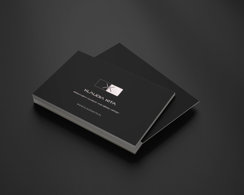 Stos wizytówek w kolorze czarnym z logo i danymi kontaktowymi firmy Klaudia Kita, specjalizującej się w makijażu permanentnym i stylizacji brwi, ułożony na ciemnym tle.