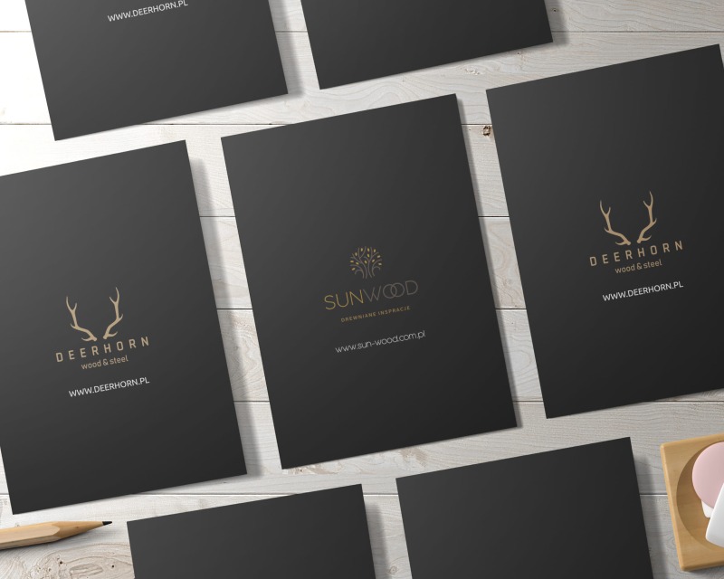 Układ czarnych wizytówek z logo firm Deerhorn i Sunwood na jasnym drewnianym tle, z ołówkiem i elementem dekoracyjnym w rogu.
