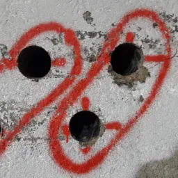 Wiercenie otworów w betonowej ścianie, zaznaczone czerwoną farbą w kształcie dwóch połączonych okręgów.