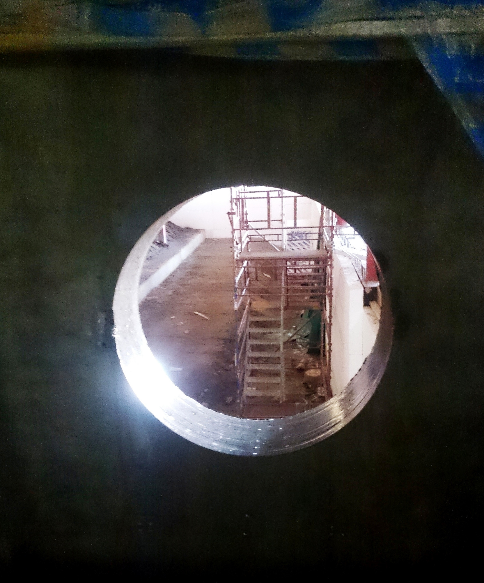 Wnętrze otworu wiertniczego z widocznym rusztowaniem i betonowym podłożem w tle, oświetlone jasnym światłem.