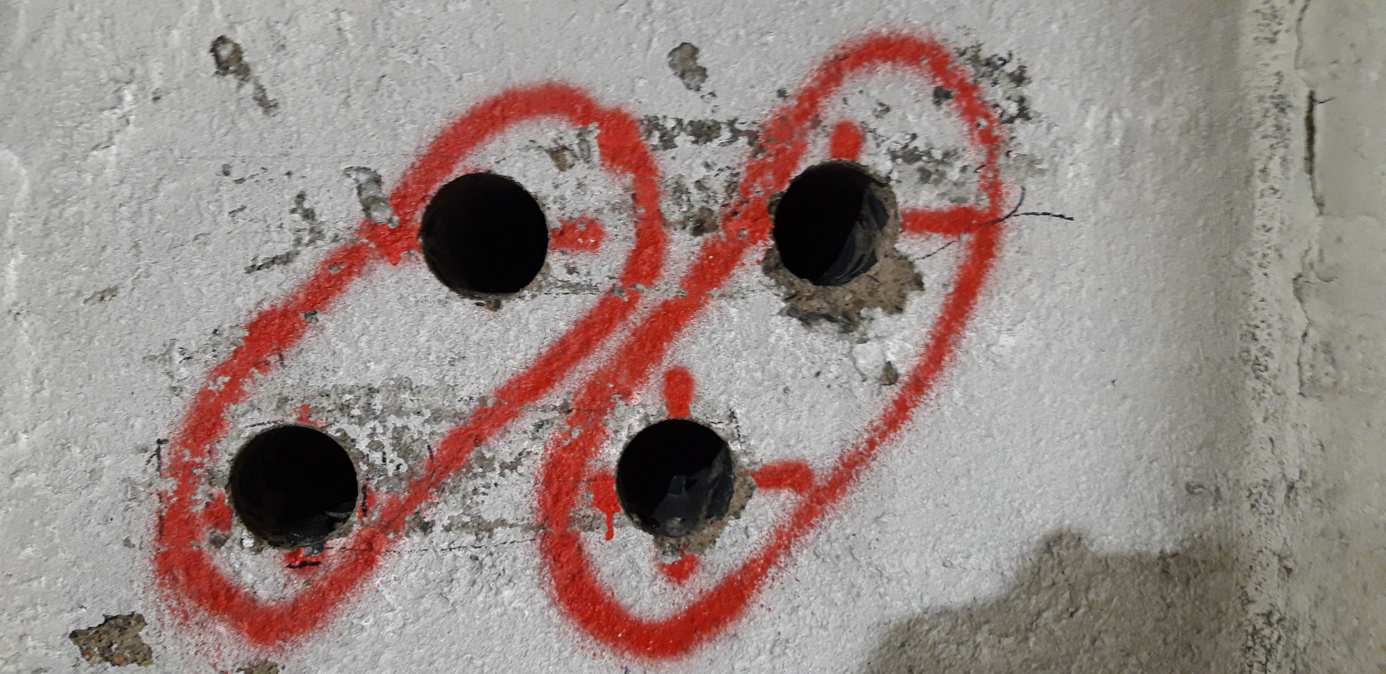 Wiercenie otworów w betonowej ścianie, zaznaczone czerwoną farbą w kształcie dwóch połączonych okręgów.