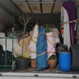 Gregor Trans - Wnętrze skrzyni ładunkowej wypełnione zabezpieczonymi przedmiotami podczas transportu, widoczne rośliny w doniczkach owinięte tkaniną i folią, rower, meble i inne przedmioty.