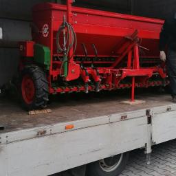 Gregor Trans - Czerwony siewnik rolniczy marki AMAZONE załadowany na platformę transportową samochodu ciężarowego z plandeką.