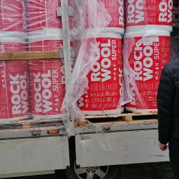 Gregor Trans - Załadunek rol izolacji Rockwool Super w opakowaniu foliowym na palecie do skrzyni ładunkowej samochodu dostawczego, widok z boku na koło i podwozie pojazdu.