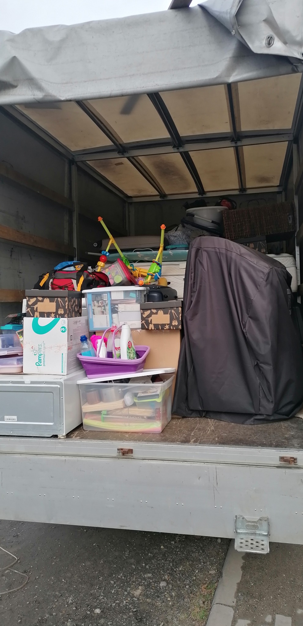 Wnętrze samochodu dostawczego wypełnione po brzegi kartonami, pudłami plastikowymi, zabawkami dziecięcymi i innymi przedmiotami gospodarstwa domowego, przygotowanymi do transportu.