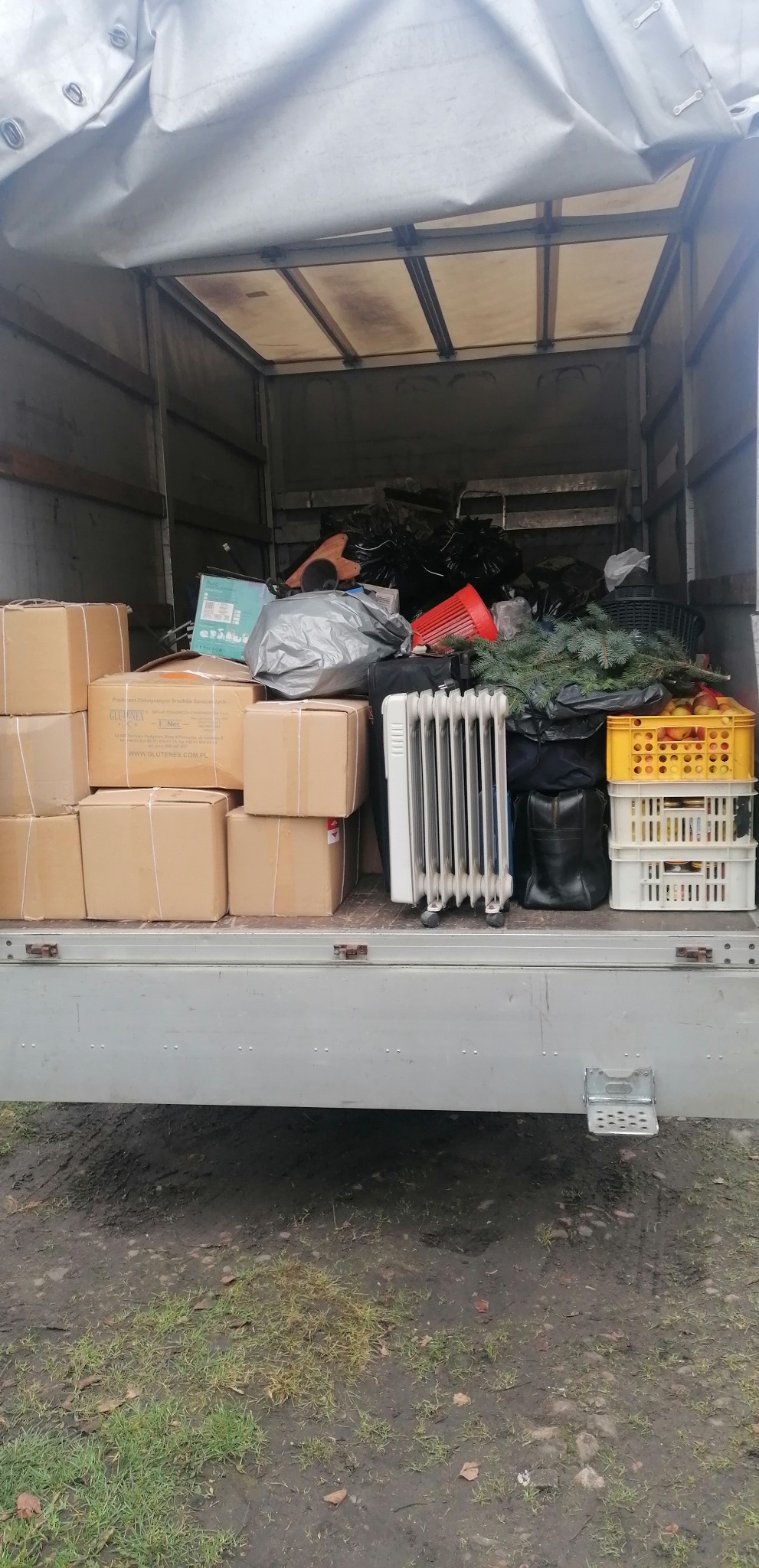 Wnętrze skrzyni ładunkowej samochodu dostawczego wypełnione kartonami, grzejnikiem olejowym, workami i innymi przedmiotami podczas załadunku.
