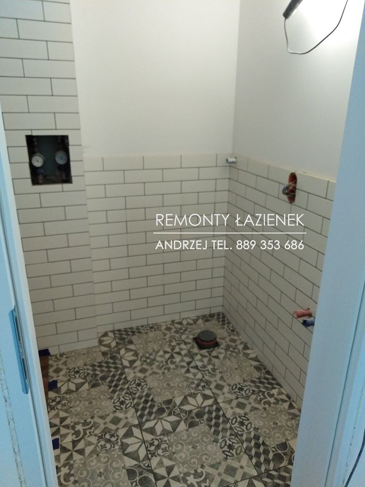 Wnętrze łazienki w trakcie remontu, widoczne białe kafelki typu metro na ścianach, wzorzysta podłoga, niezabudowane rury i otwór rewizyjny.