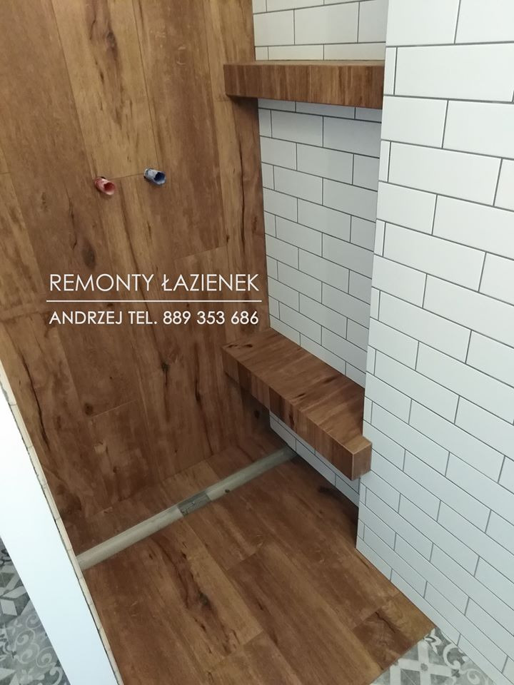 Wnętrze prysznica w trakcie wykańczania: imitacja drewna na ścianach i podłodze, półki z litego drewna, białe, prostokątne płytki ułożone cegiełkowo na ścianie. Widoczne rury i przyłącza wodne.