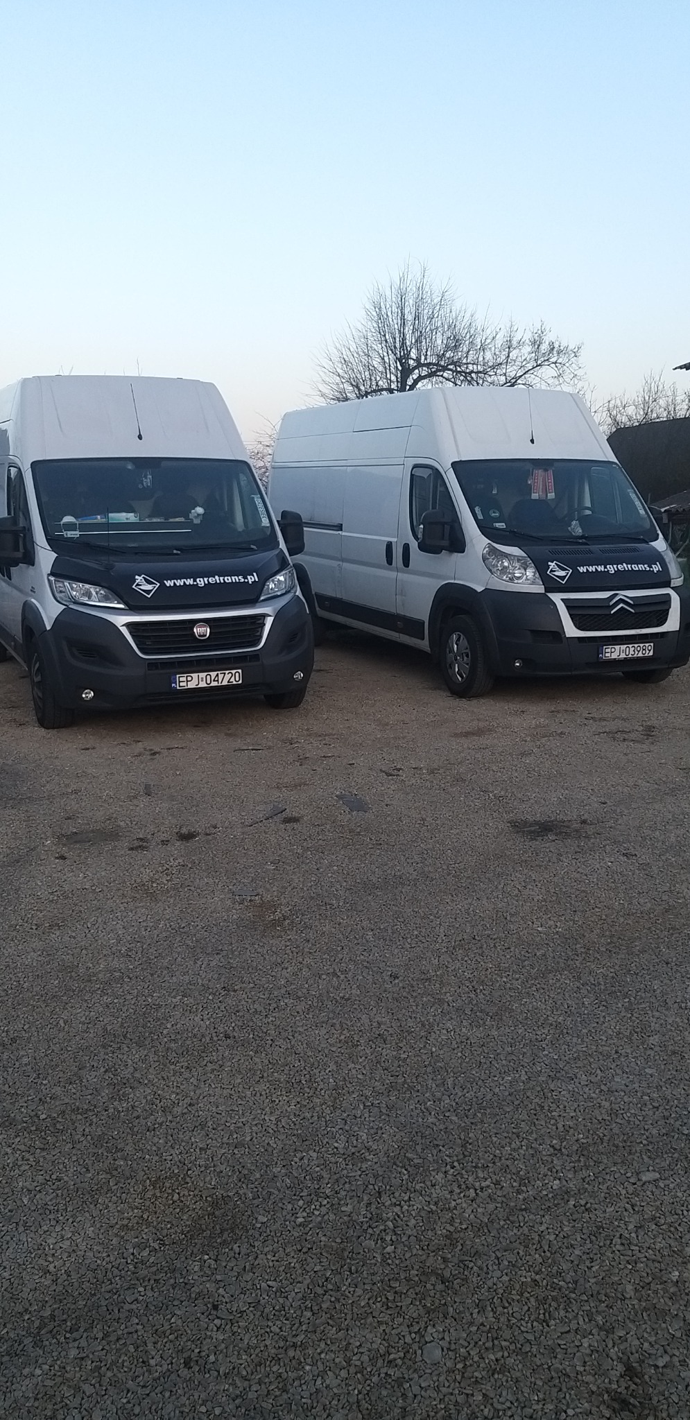 Dwa białe busy dostawcze firmy transportowej Gretrans zaparkowane na żwirowym parkingu, widoczne tablice rejestracyjne i logo firmy na masce.