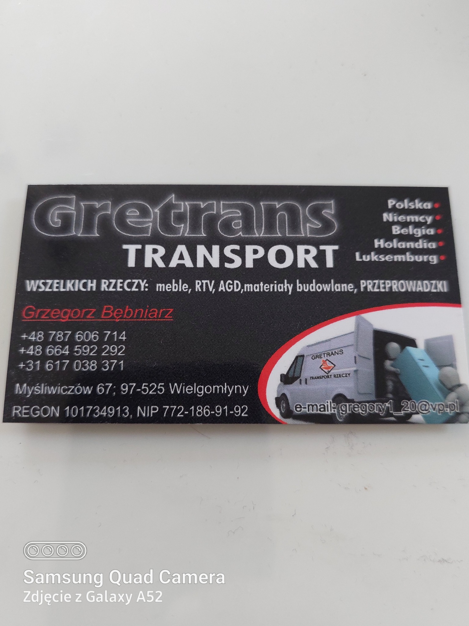 Wizytówka firmy transportowej Grettrans z logo, numerami telefonów i adresem e-mail. Na wizytówce widnieje grafika przedstawiająca samochód dostawczy podczas załadunku mebli.