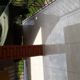 Wyłożony jasnymi, beżowymi płytkami balkon z ceglanym filarem i metalową balustradą, widok z góry pod kątem.