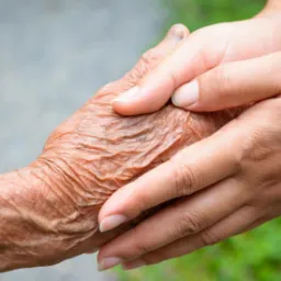 Dłoń osoby starszej spoczywająca w dłoni osoby młodszej, ukazująca troskę i wsparcie.