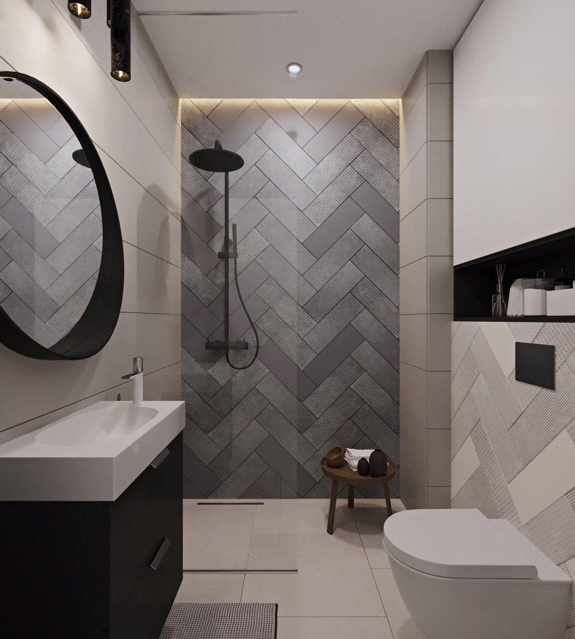 Nowoczesna łazienka w Gdańsku z szarymi płytkami ułożonymi w jodełkę na ścianie prysznicowej, okrągłe lustro z czarną ramą nad białą umywalką i czarną szafką, minimalistyczny design.
