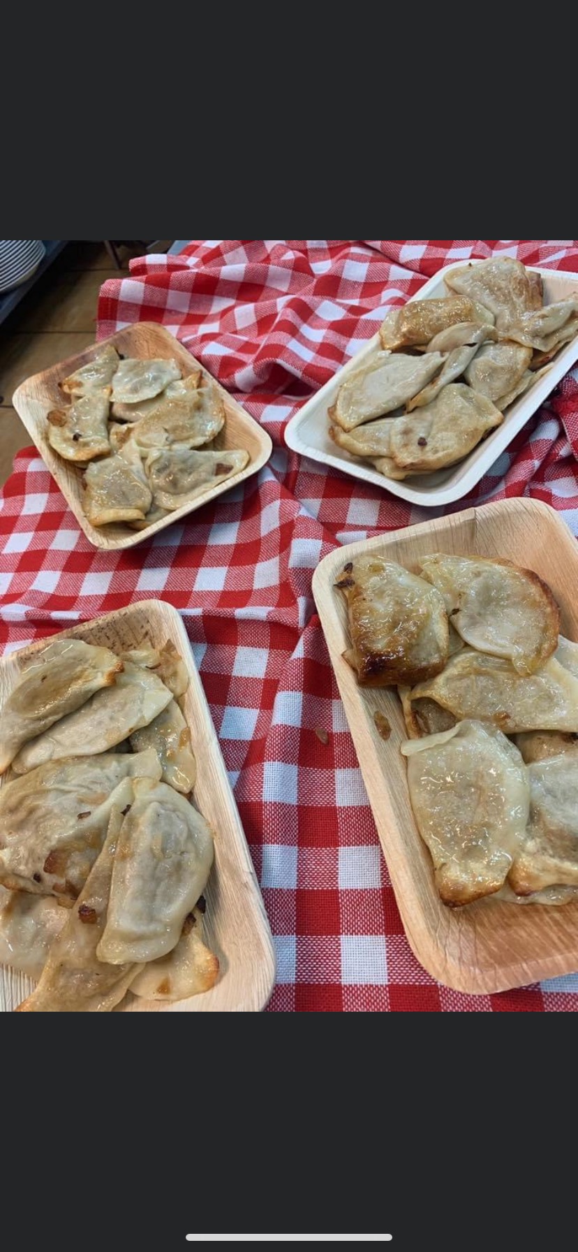 Cztery drewniane tacki z podsmażanymi pierogami na czerwono-białej kraciastej serwecie, widok z góry.