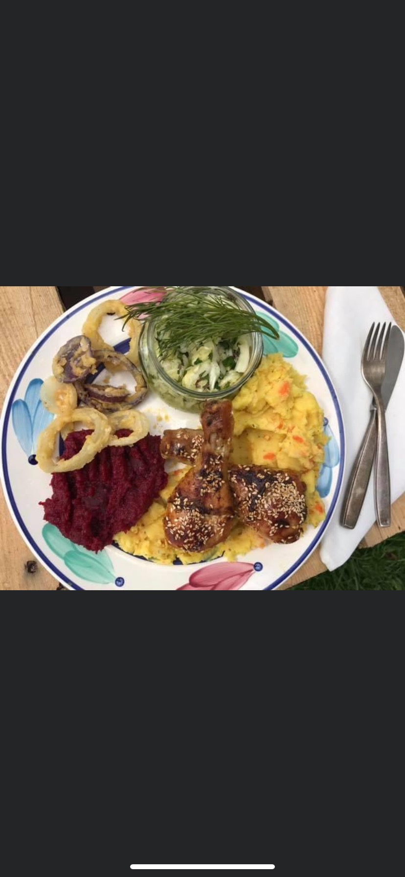 Dekoracyjny talerz z pieczonym kurczakiem posypanym sezamem, puree z buraków, puree z marchewki, sałatką w słoiku i smażonymi krążkami cebuli.