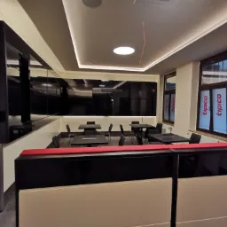 Nowoczesne wnętrze biurowe z czarnymi meblami, oświetleniem LED i oknami z logo firmy, widoczne niedokończone okablowanie sufitowe.