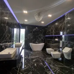 Luksusowa łazienka z czarnymi marmurowymi płytkami, wolnostojącą białą wanną, podwieszanymi umywalkami, toaletą i bidetem, oświetleniem LED oraz kryształowym żyrandolem.
