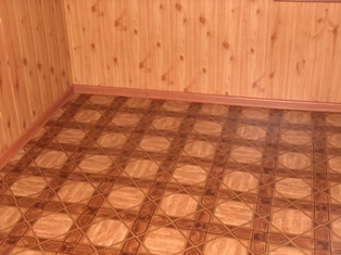 Wnętrze pokoju wykończone boazerią na ścianach i wzorzystą, brązowo-beżową podłogą z paneli. Widoczny narożnik pomieszczenia z listwą przypodłogową.