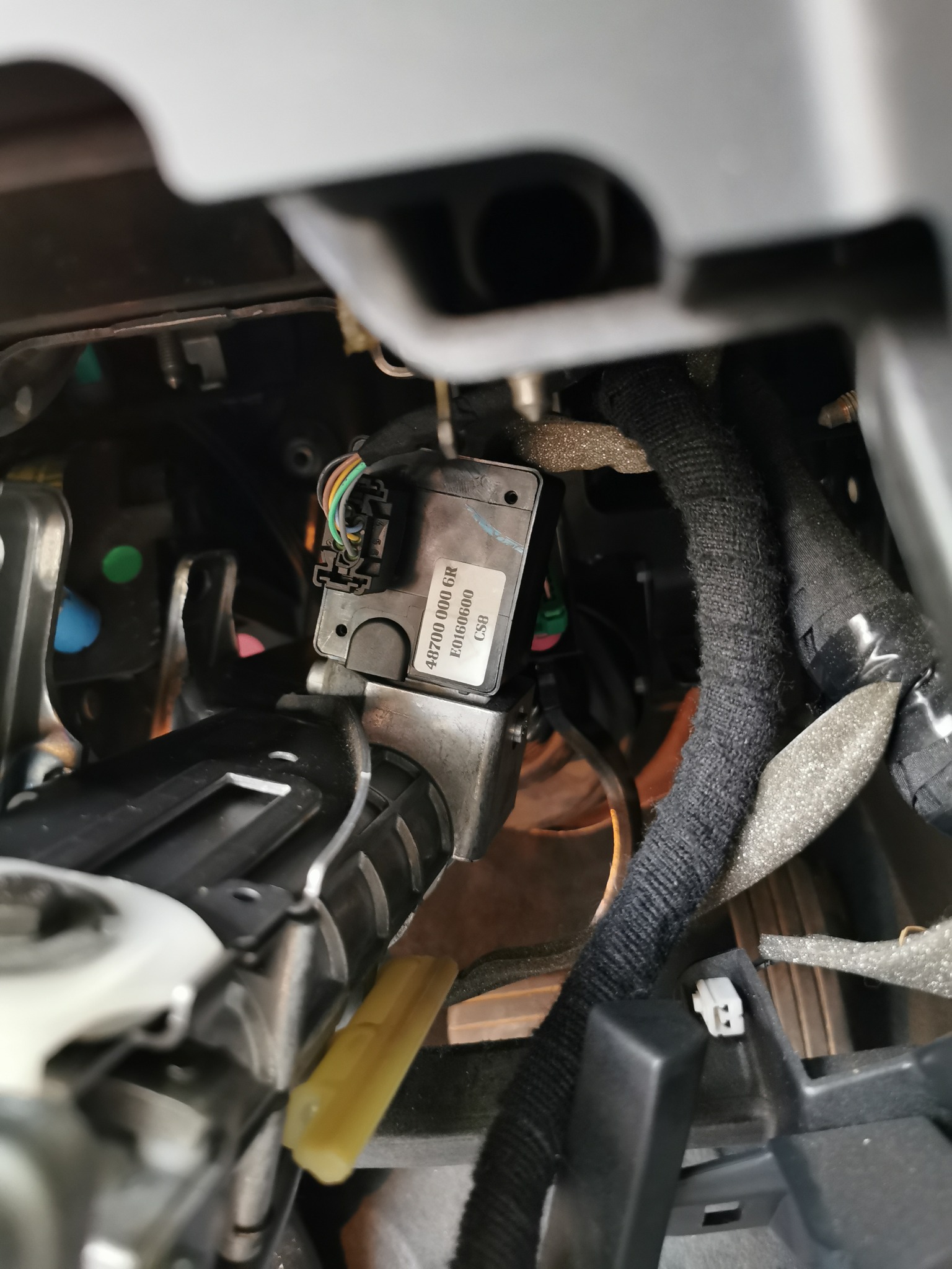 Wnętrze samochodu z widocznym modułem elektronicznym z numerem seryjnym i wiązką przewodów w osłonie, zamontowany pod deską rozdzielczą.