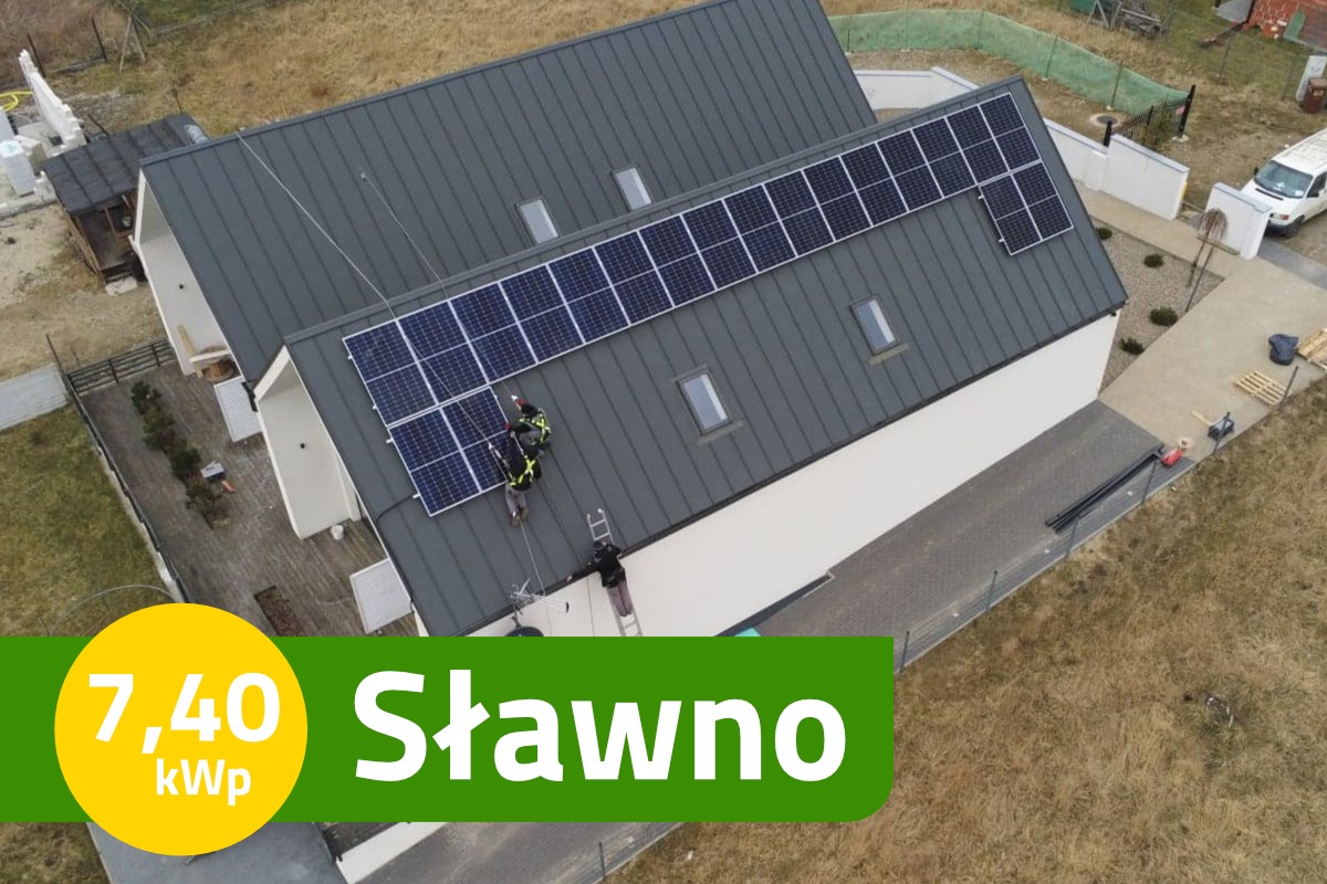 Montaż paneli słonecznych na dachu domu jednorodzinnego z szarej blachy, dwóch monterów w uprzężach zabezpieczających, widok z góry.