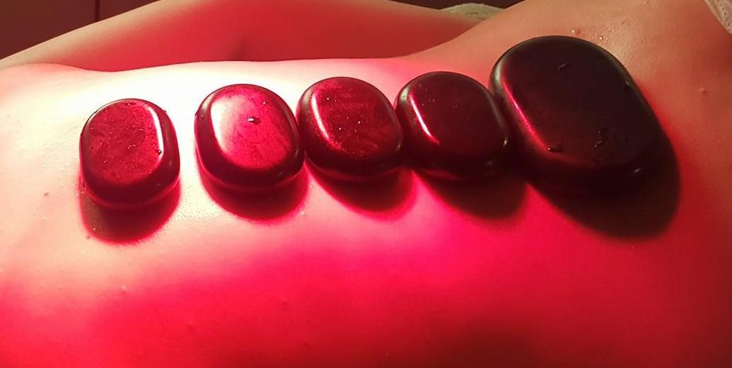 Pięć gładkich, ciemnych kamieni ułożonych wzdłuż kręgosłupa pacjenta, oświetlonych czerwonym światłem podczas zabiegu relaksacyjnego.