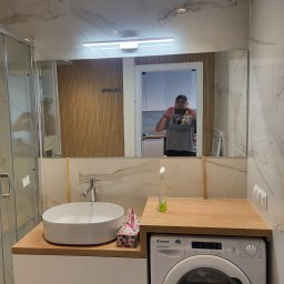ZANE DESIGN SPÓŁKA Z OGRANICZONĄ ODPOWIEDZIALNOŚCIĄ - Nowoczesna łazienka z marmurowymi płytkami, kabiną prysznicową, umywalką nablatową i pralką pod blatem, sfotografowana z odbiciem osoby robiącej zdjęcie w lustrze.