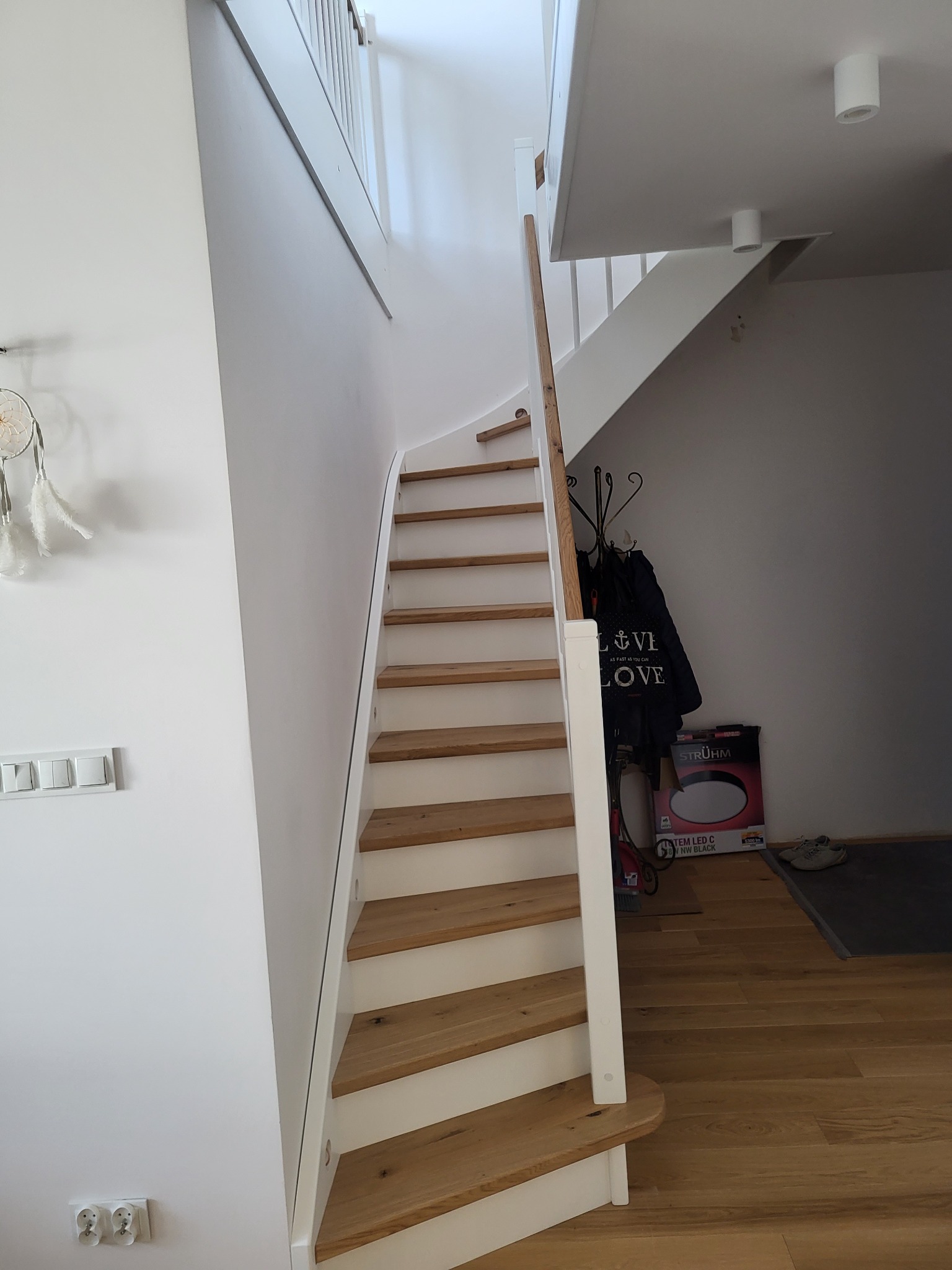 Nowe schody drewniane z białymi podstopnicami w jasnym wnętrzu, widok z dołu, na ścianie wisi łapacz snów.
