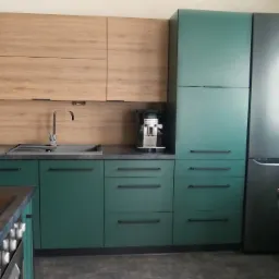 Nowoczesna kuchnia z zielonymi szafkami dolnymi i drewnopodobnymi górnymi, szarym blatem, srebrnym kranem i ekspresem do kawy.