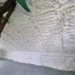 Poddasze ocieplone białą pianką poliuretanową, widoczne drewniane elementy konstrukcyjne pomalowane na zielono i brązowo, ciemna podłoga.