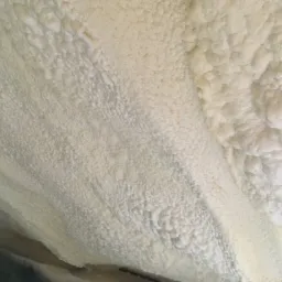 Szczegółowe ujęcie nierównej powierzchni jasnej pianki izolacyjnej na poddaszu, z widocznymi strukturami komórkowymi i delikatnymi cieniami.