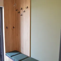 Wnęka z siedziskiem obitym zielonym welurem, drewnianą boazerią z wieszakami i wystającym kablem od lampki.