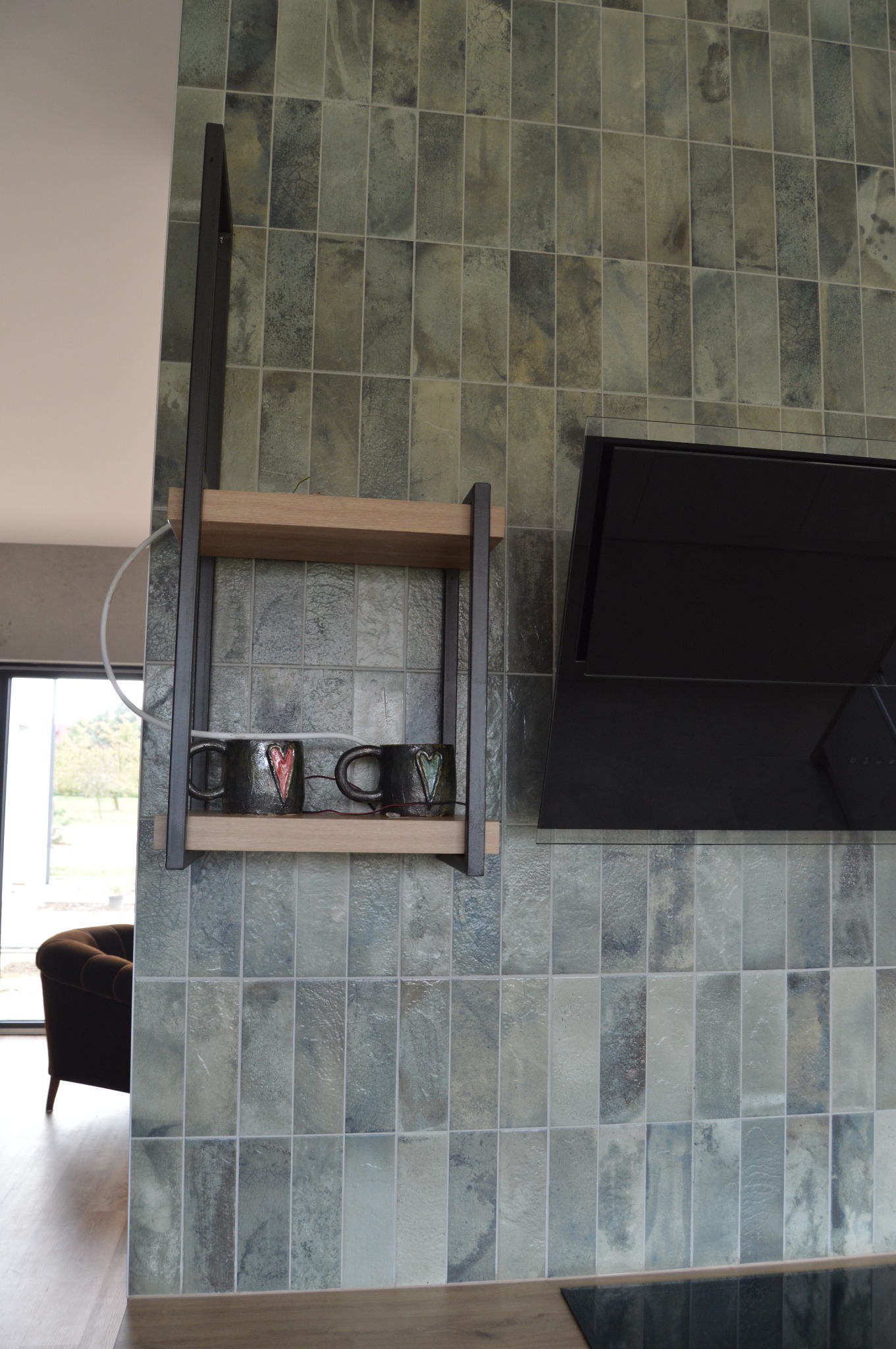 Fragment kuchni z płytkami imitującymi kamień, na ścianie półka z dwiema ceramicznymi filiżankami z motywem serca, obok czarny okap kuchenny.