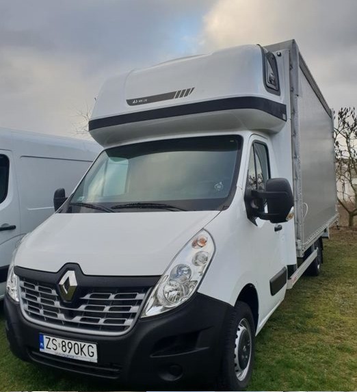 Biały samochód dostawczy Renault Master z wysoką zabudową i plandeką, zaparkowany na trawie, widoczne tablice rejestracyjne ZS 890KG.