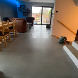 Szare płytki podłogowe w salonie z widokiem na ogród w Iławie. Widoczne narzędzia i resztki po pracy przy schodach.