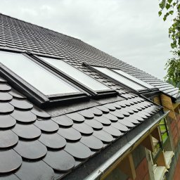 Rafał Sobkowiak - Dach pokryty ciemną dachówką bitumiczną w kształcie łuski, z trzema oknami dachowymi. Widoczny fragment rynny i elewacji w trakcie wykończenia.