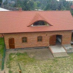 Rafał Sobkowiak - Ceglany budynek z nowym dachem z dachówki ceramicznej w odcieniach czerwieni, z oknem w kształcie łuku na poddaszu. Widok z góry, otoczenie zielone.