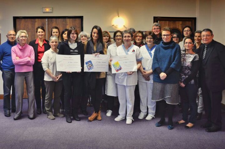 Grupa osób trzymająca dyplomy na tle drewnianych drzwi i fioletowej wykładziny.