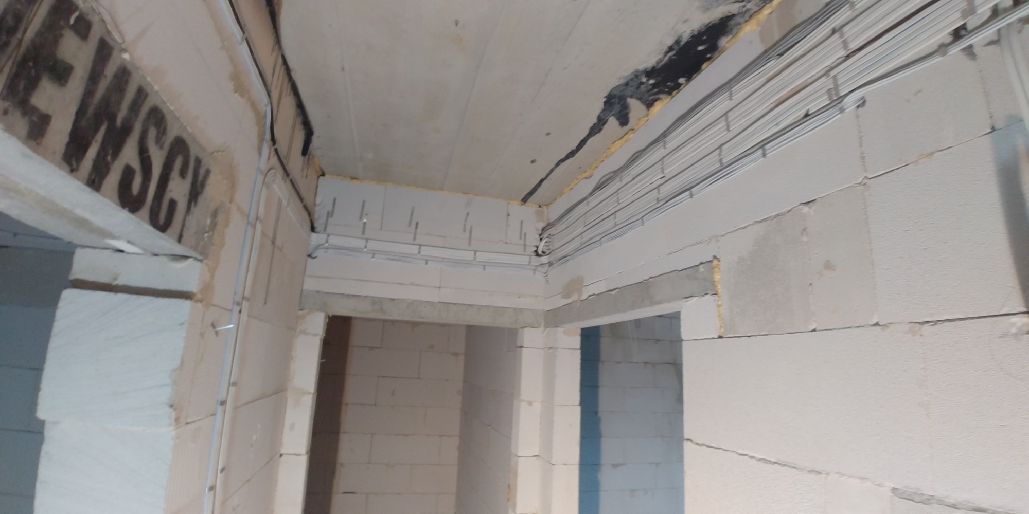 Wewnętrzne ściany z betonu komórkowego w trakcie budowy z widocznymi przewodami elektrycznymi ułożonymi pod sufitem.