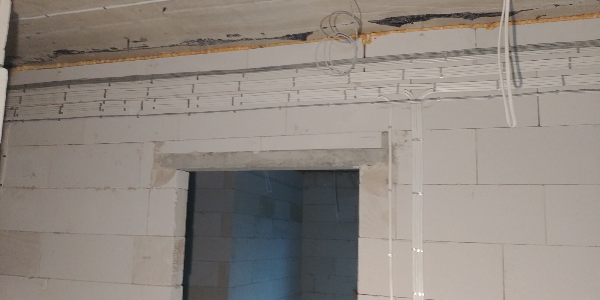 Wewnętrzne rozprowadzenie przewodów elektrycznych w surowym stanie budynku w Wejherowie, widoczne kable mocowane do ściany z betonu komórkowego oraz przewody pod sufitem zabezpieczone pianką...