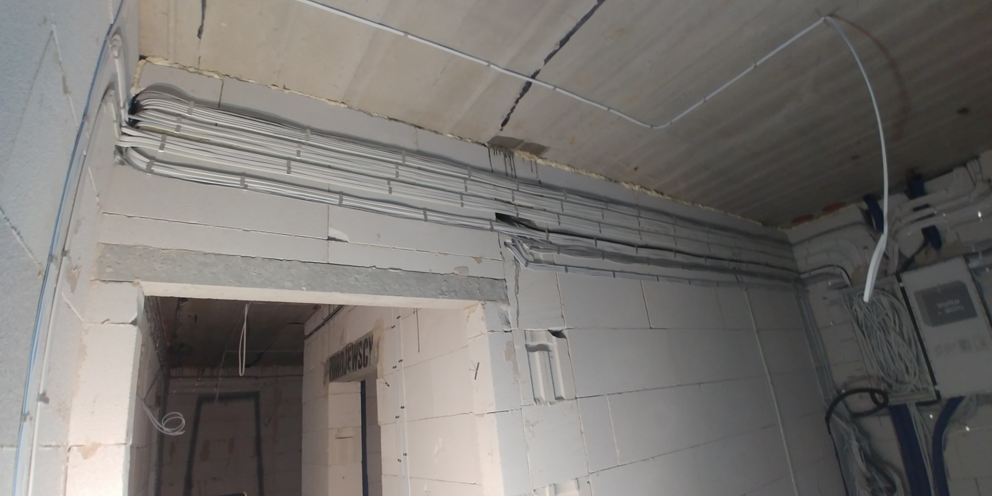 Wnętrze w trakcie remontu z widoczną instalacją elektryczną w korytach i przewodach prowadzonych po ścianach z betonu komórkowego oraz pod sufitem.