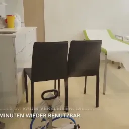 Zamgławianie pomieszczenia: widok na wnętrze gabinetu z dwoma krzesłami, leżanką z białym prześcieradłem i urządzeniem do zamgławiania na podłodze.