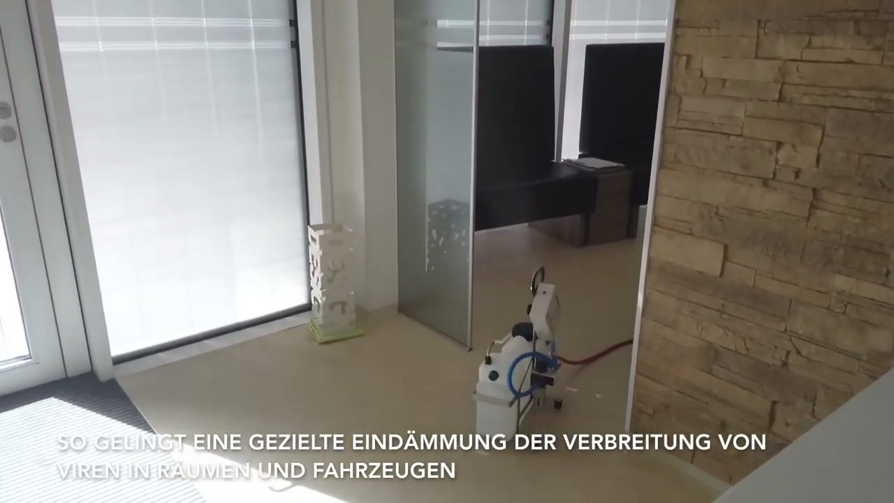 Zamgławianie pomieszczenia biurowego przy użyciu urządzenia Pfalz Tec. Widoczna ściana z imitacji kamienia, przeszklone biuro i rolety w oknach.