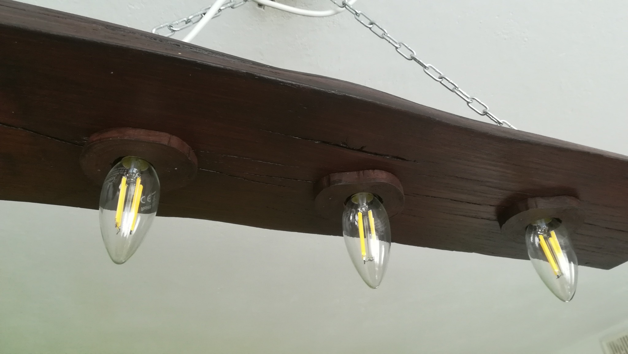 Drewniana belka z trzema żarówkami LED w stylu retro, zawieszona na metalowym łańcuchu, oświetlenie wewnętrzne.