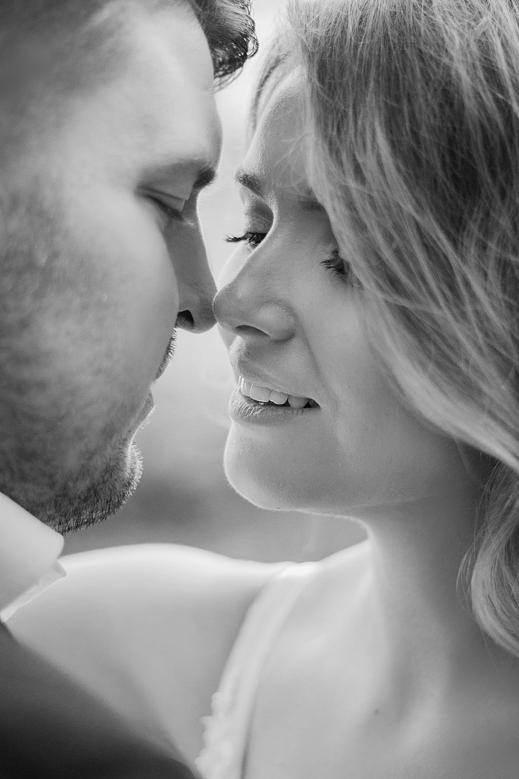 Czarno-białe zbliżenie profilu pary młodej: panna młoda z delikatnym uśmiechem i długimi rzęsami, pan młody z krótkim zarostem, ich nosy prawie się dotykają.