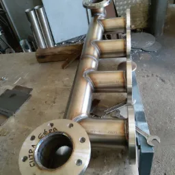 Poskładana konstrukcja rurowa ze stali nierdzewnej z widocznymi spawami i kołnierzami, leżąca na warsztatowym stole, obok narzędzi.