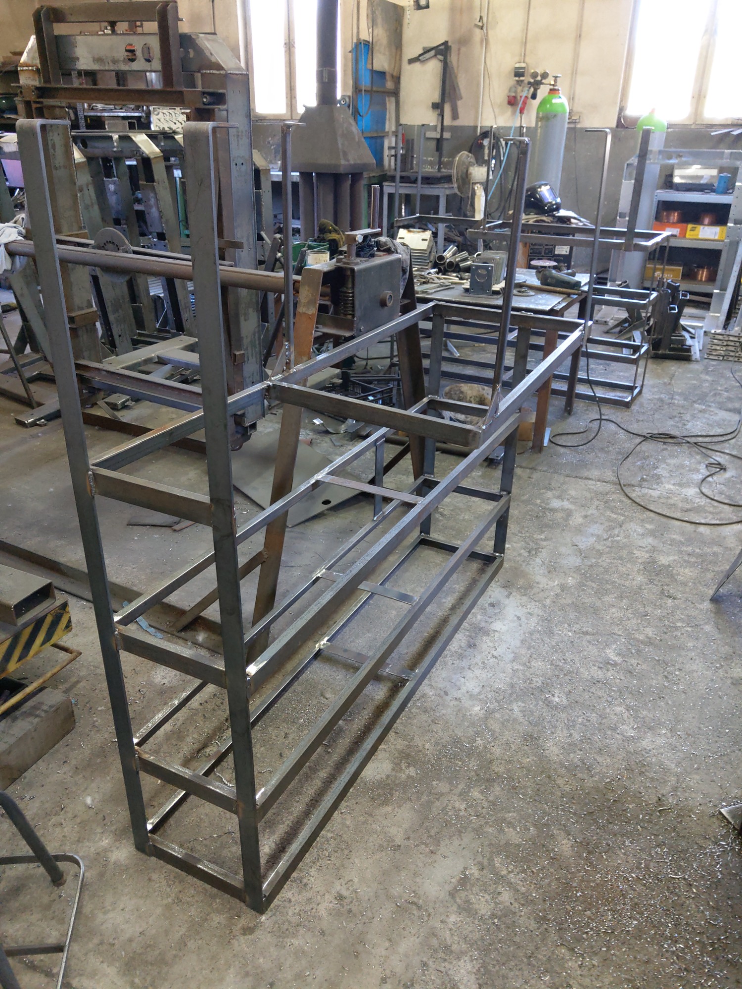 Metalowa konstrukcja ramowa z profili kwadratowych, spawana, w warsztacie, widoczne ślady obróbki i spawania, surowe wykończenie.